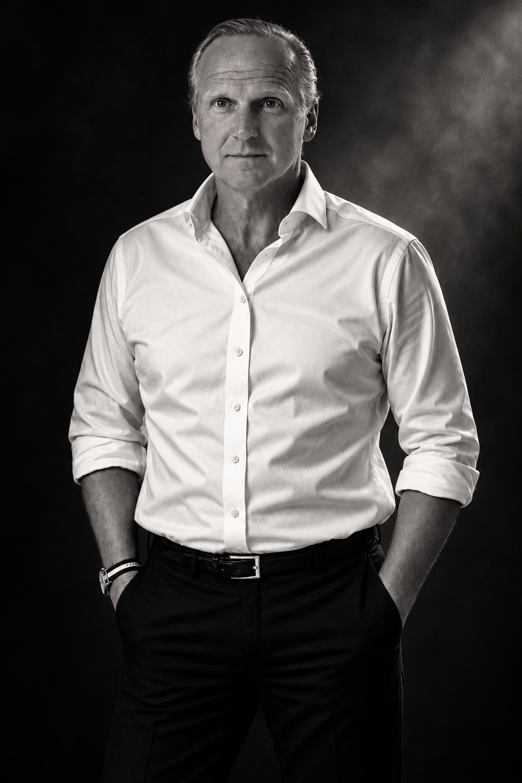 Bernd Johannes Wuebben, standing in a white shirt against a dark background, photographed in black and white